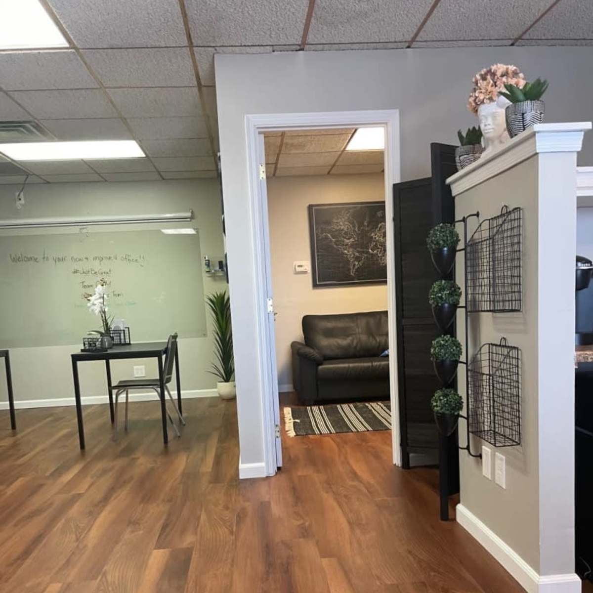 A welcoming office space with a wooden floor, including a table and chairs on one side and a black couch in the adjacent room.