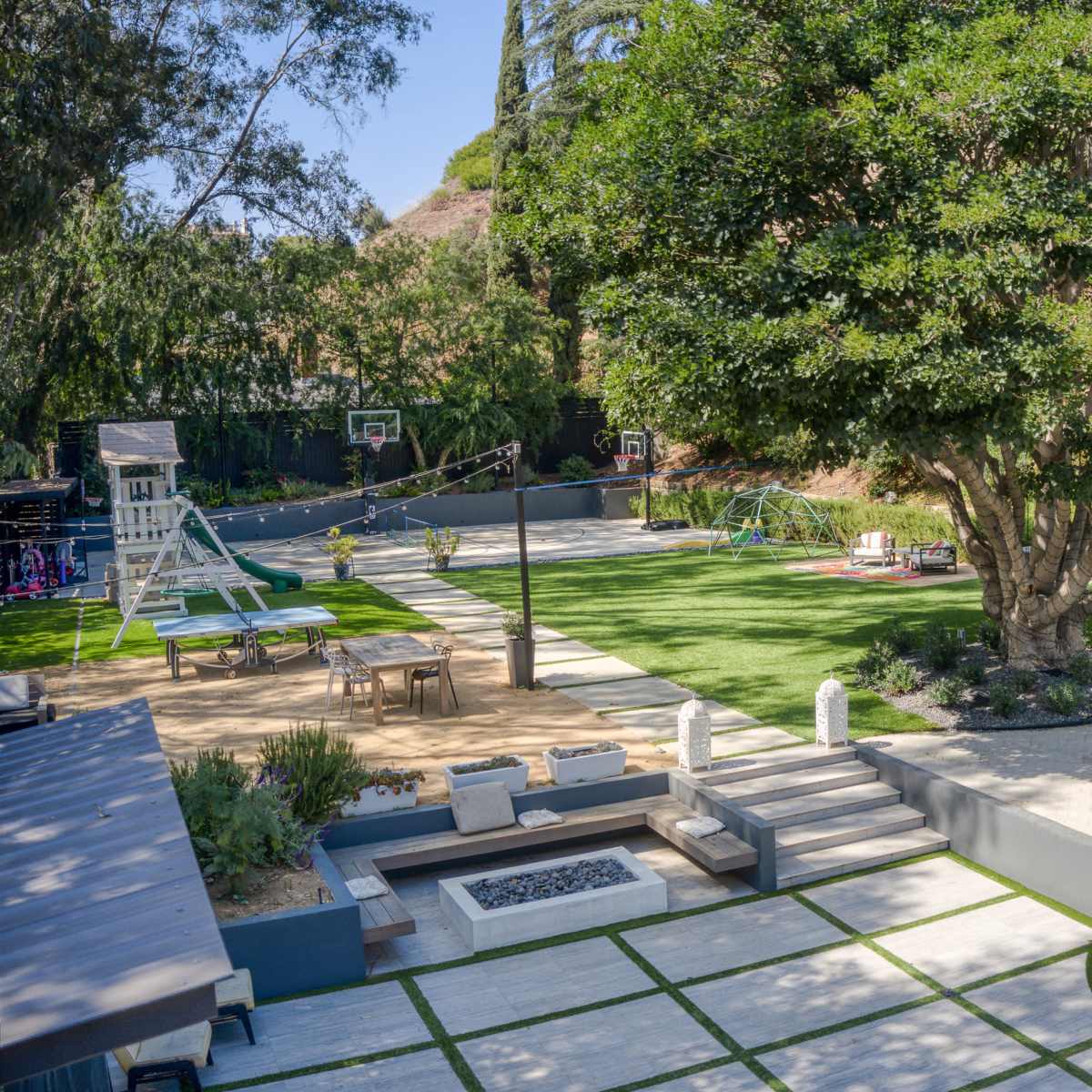 A spacious backyard featuring a pool, seating area, playground equipment, and a large tree, with various recreational spaces and landscaping.