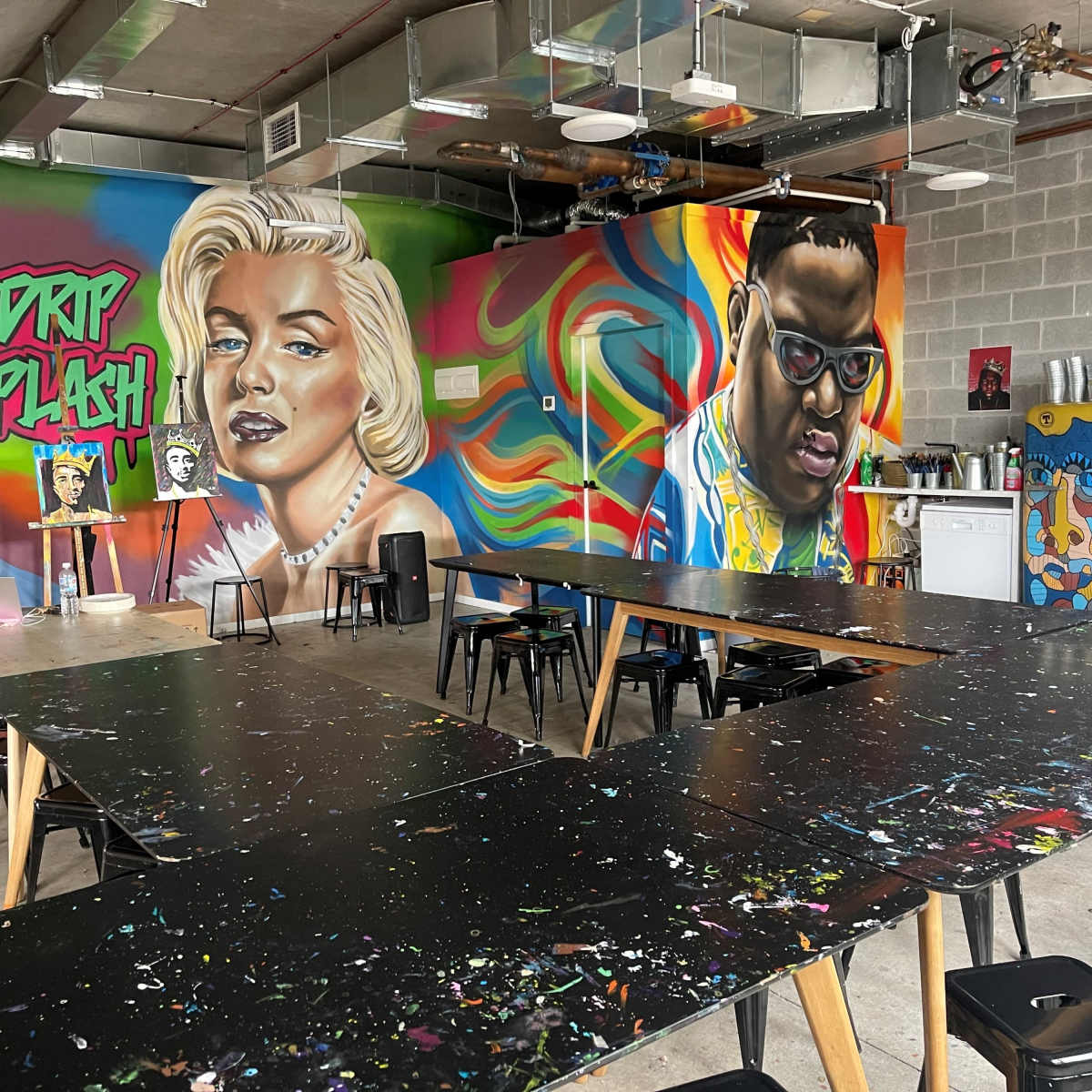 An art studio with several long tables and colorful murals of famous figures on the walls.