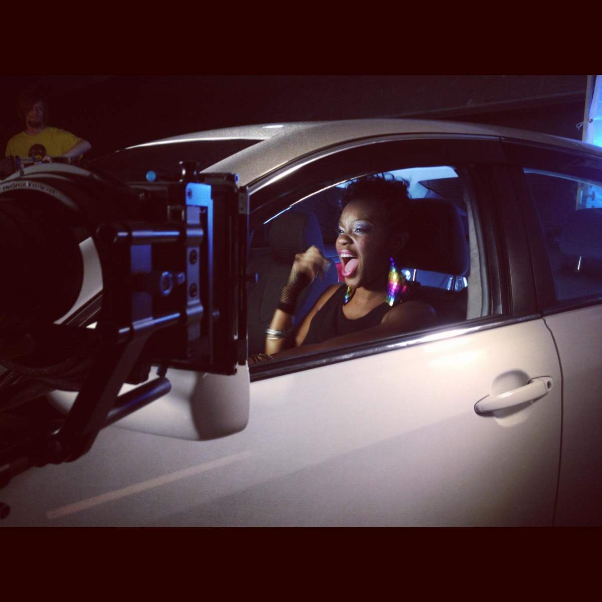 A woman is laughing inside a car while a camera is positioned in front of her.