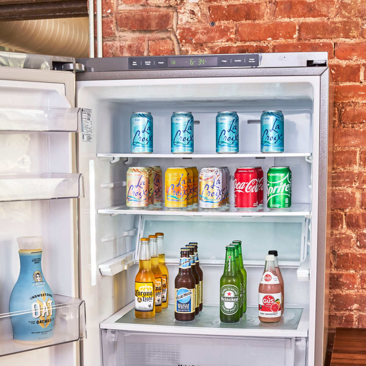 An open refrigerator filled with various cans of soda and bottles of drinks on its shelves.