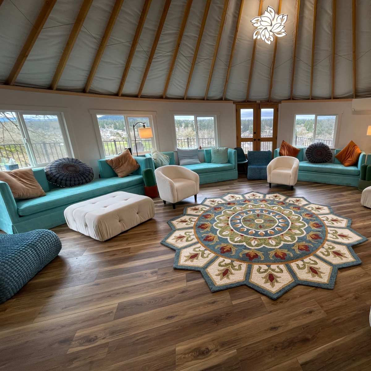 A round, airy lounge space with turquoise sofas, white armchairs, and a large, decorative area rug at the center.