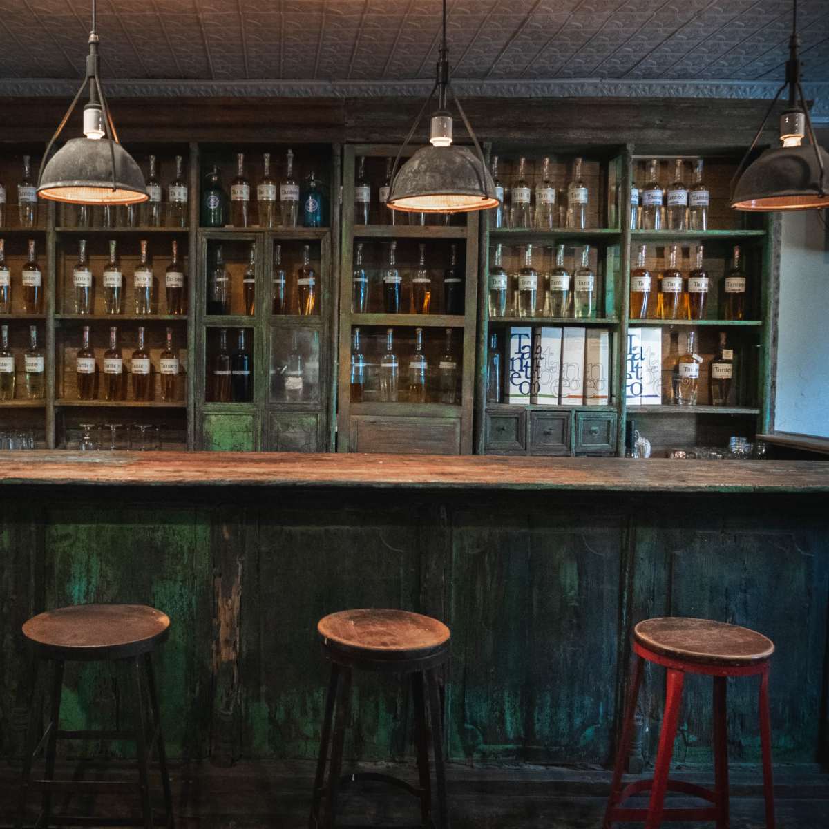 A rustic bar feature with a wooden counter and shelves lined with glass bottles in a dimly lit room.