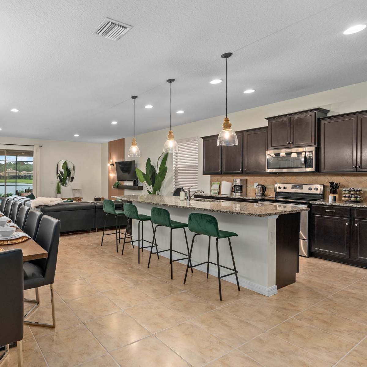 A spacious dining area with a long table set for a meal, adjacent to a modern kitchen with a large island and bar stools.