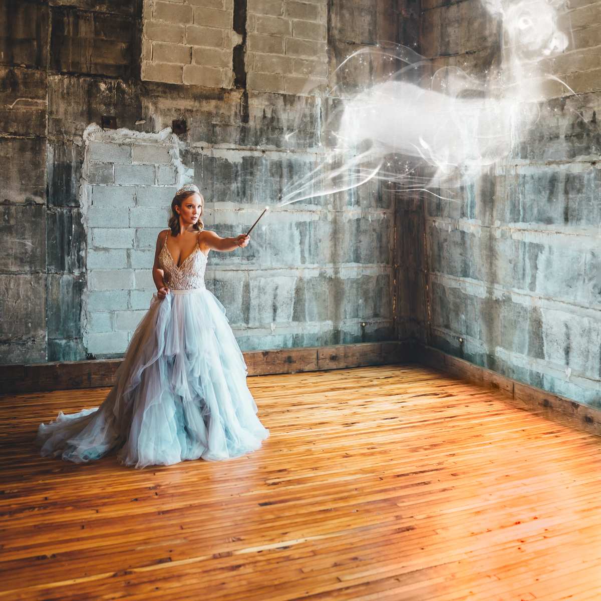 A woman in a flowing dress casts a spell, creating a translucent deer in an empty, rustic room with wooden floors and concrete walls.