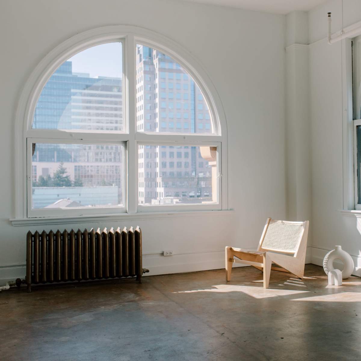 A minimalist room with large arched windows, a wooden chair, and a couple of decorative white vases.