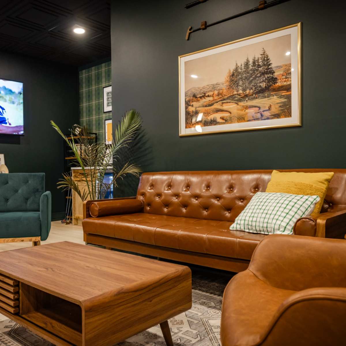 A cozy living room with a brown leather sofa, two chairs, a wooden coffee table, and a television displaying a sports scene against a dark green wall.