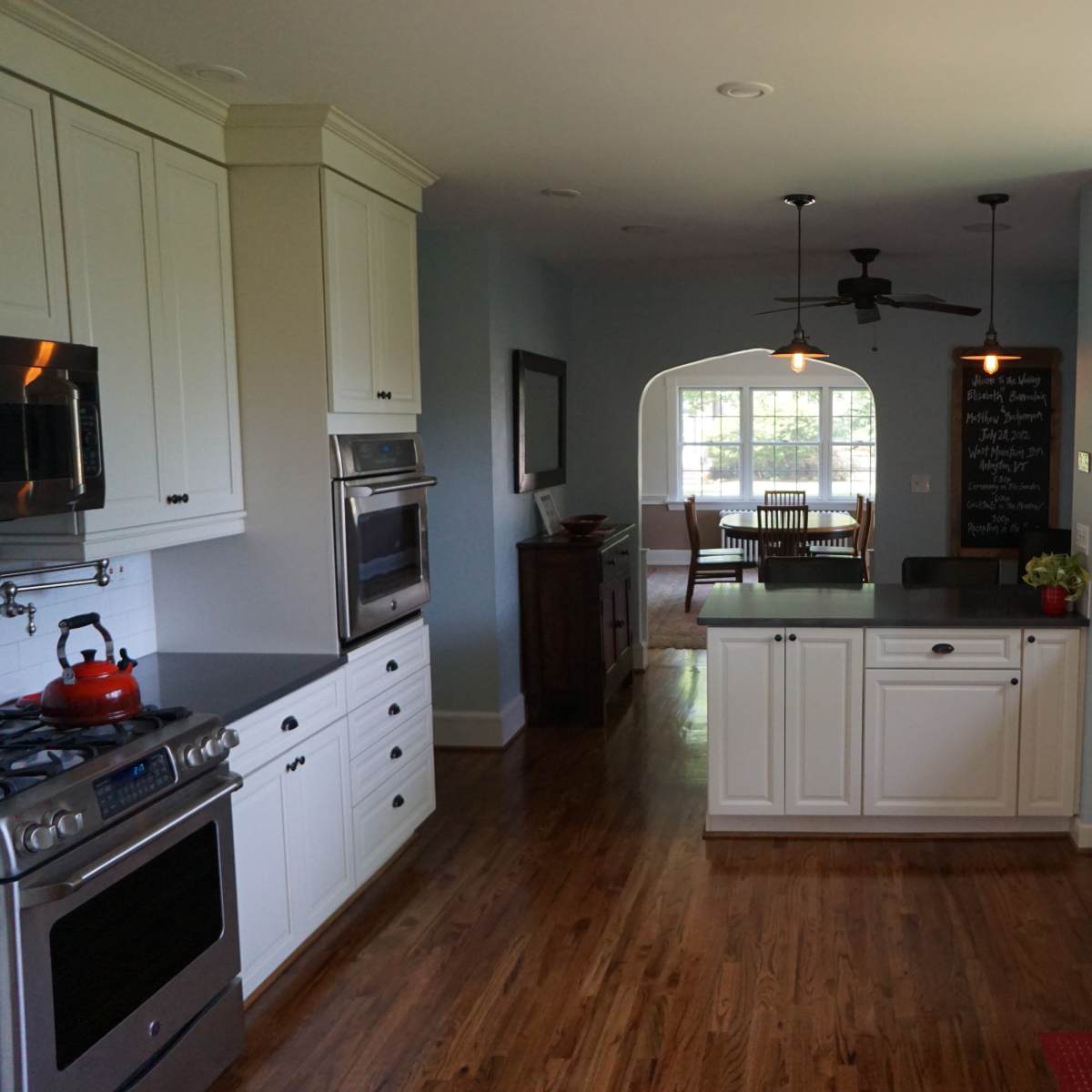 A modern kitchen featuring white cabinets, stainless steel appliances, and a view into a dining area through an arched doorway.