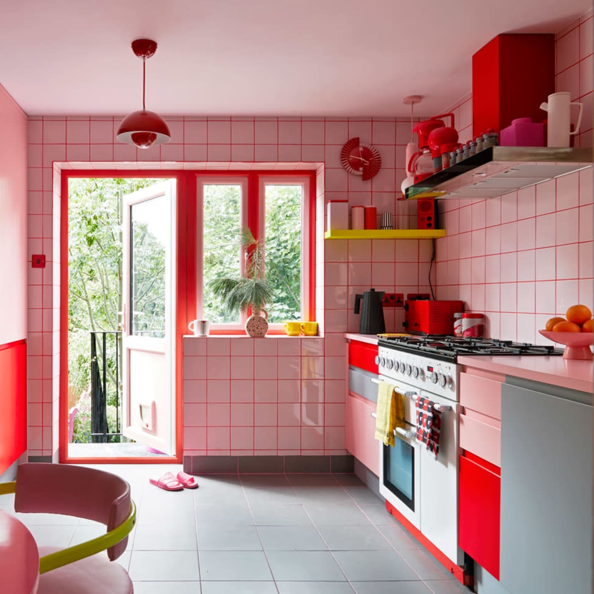 A bright kitchen features red and pink tiles, modern appliances, and a view of greenery through a large window.