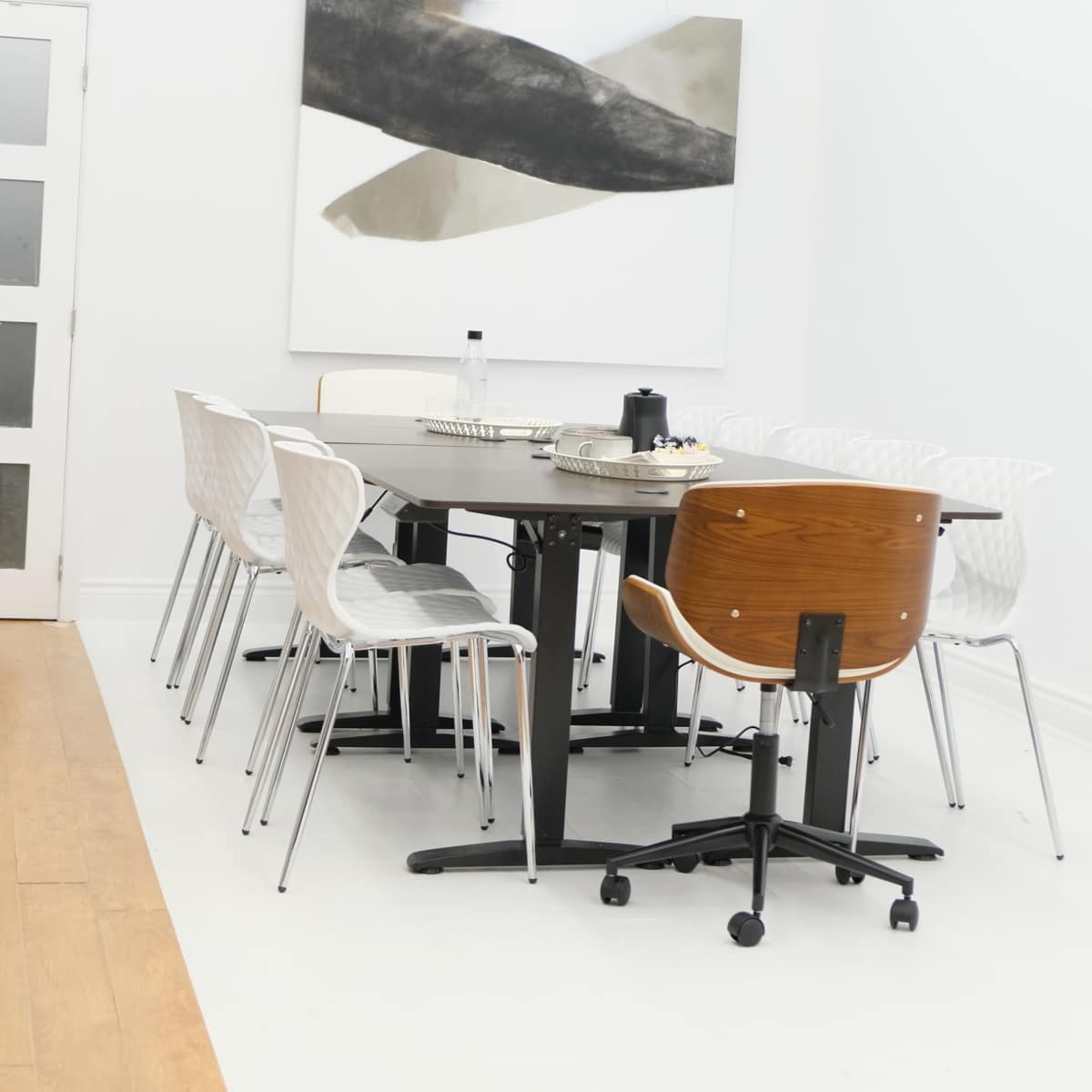 A modern dining area features a round black table surrounded by white and wooden chairs, with a large abstract painting on the wall.