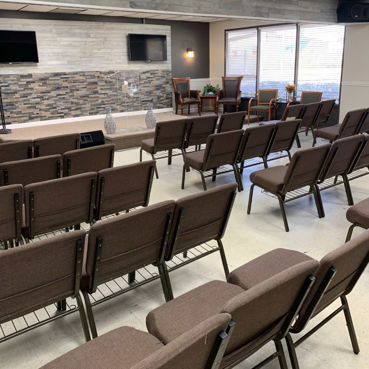 A seating arrangement in a room with brown chairs facing a stage area that features a stone wall and two wooden chairs.