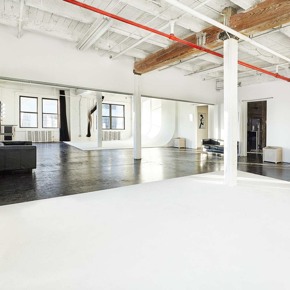 A spacious, empty studio with white walls, exposed wooden beams, and large mirrors.
