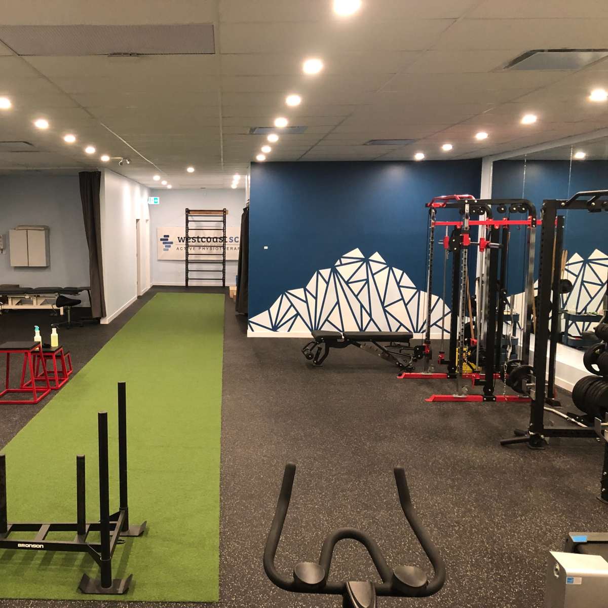 A fitness gym with various workout equipment, including weights, benches, and a green turf area for exercises.
