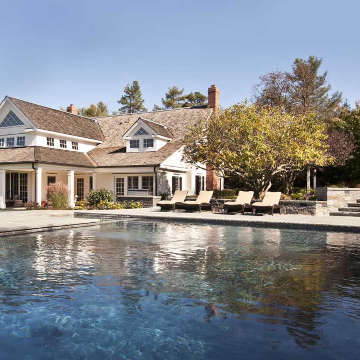 A spacious house with a backyard pool surrounded by lounge chairs and landscaped trees.