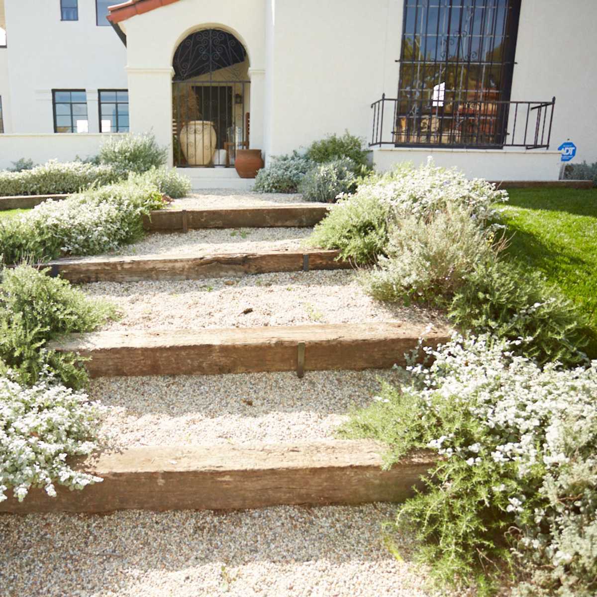 A pathway of wooden steps leads through landscaped greenery to the entrance of a white building.