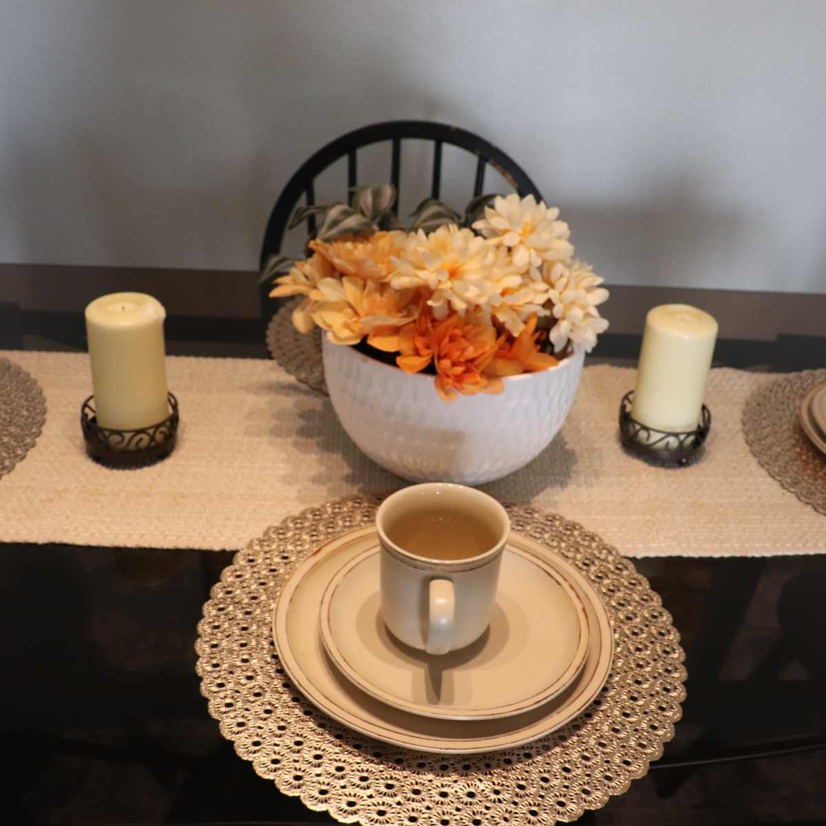 A dining table is set with four place settings, each featuring a plate and cup, along with a decorative bowl of flowers and candles in the center.