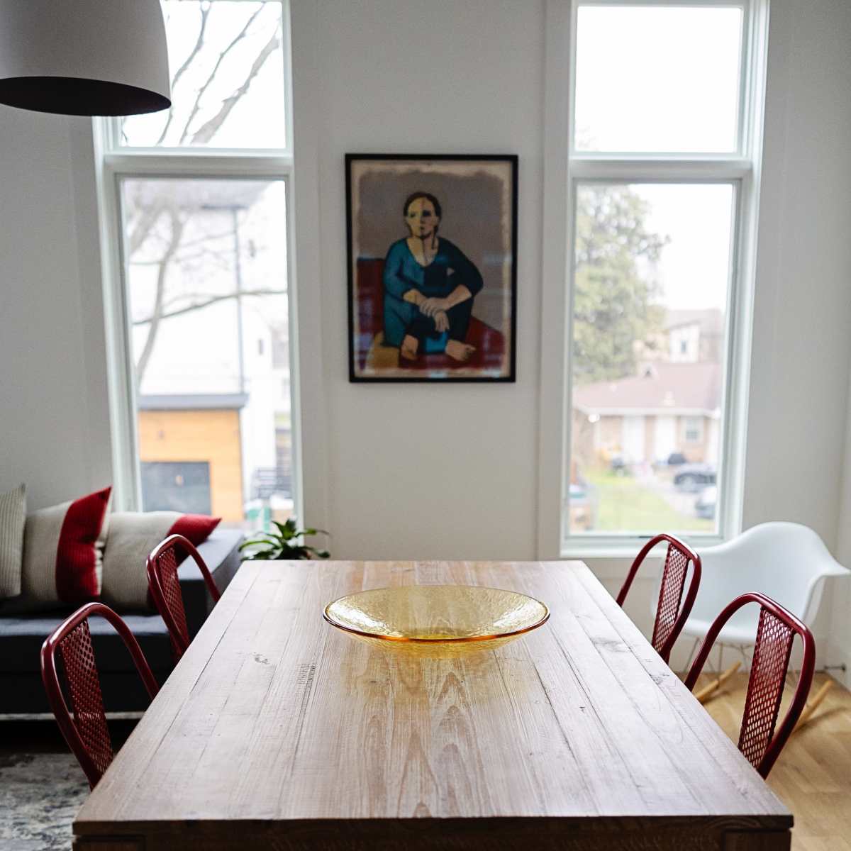 A wooden dining table is set in a room with large windows, surrounded by red chairs, and features a decorative bowl in the center.