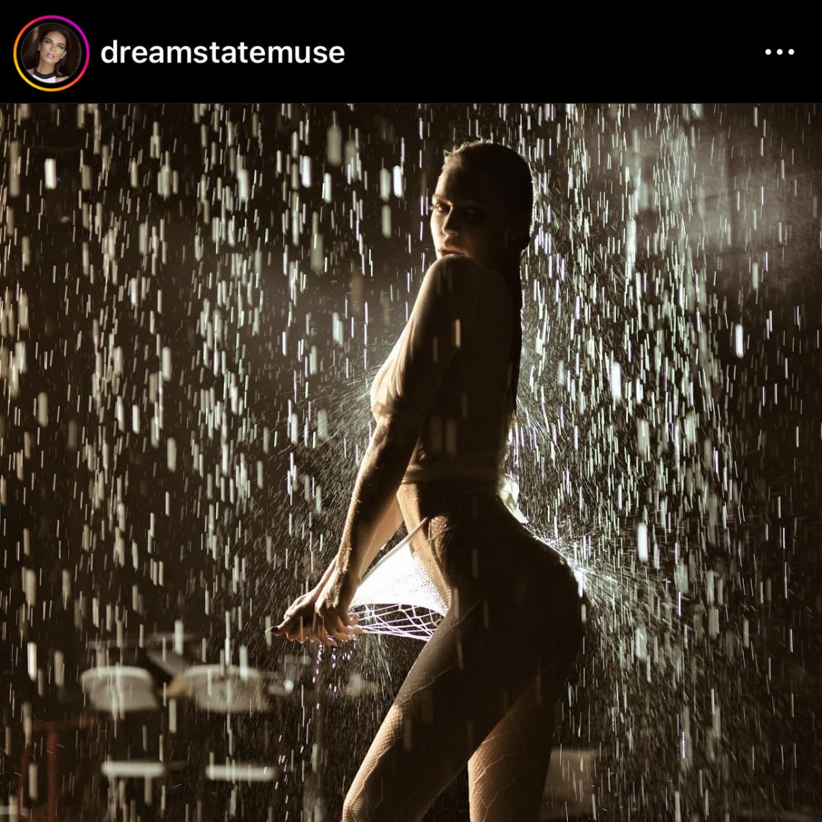 A silhouette of a person stands under a waterfall, with water cascading around them in a dramatic light setting.