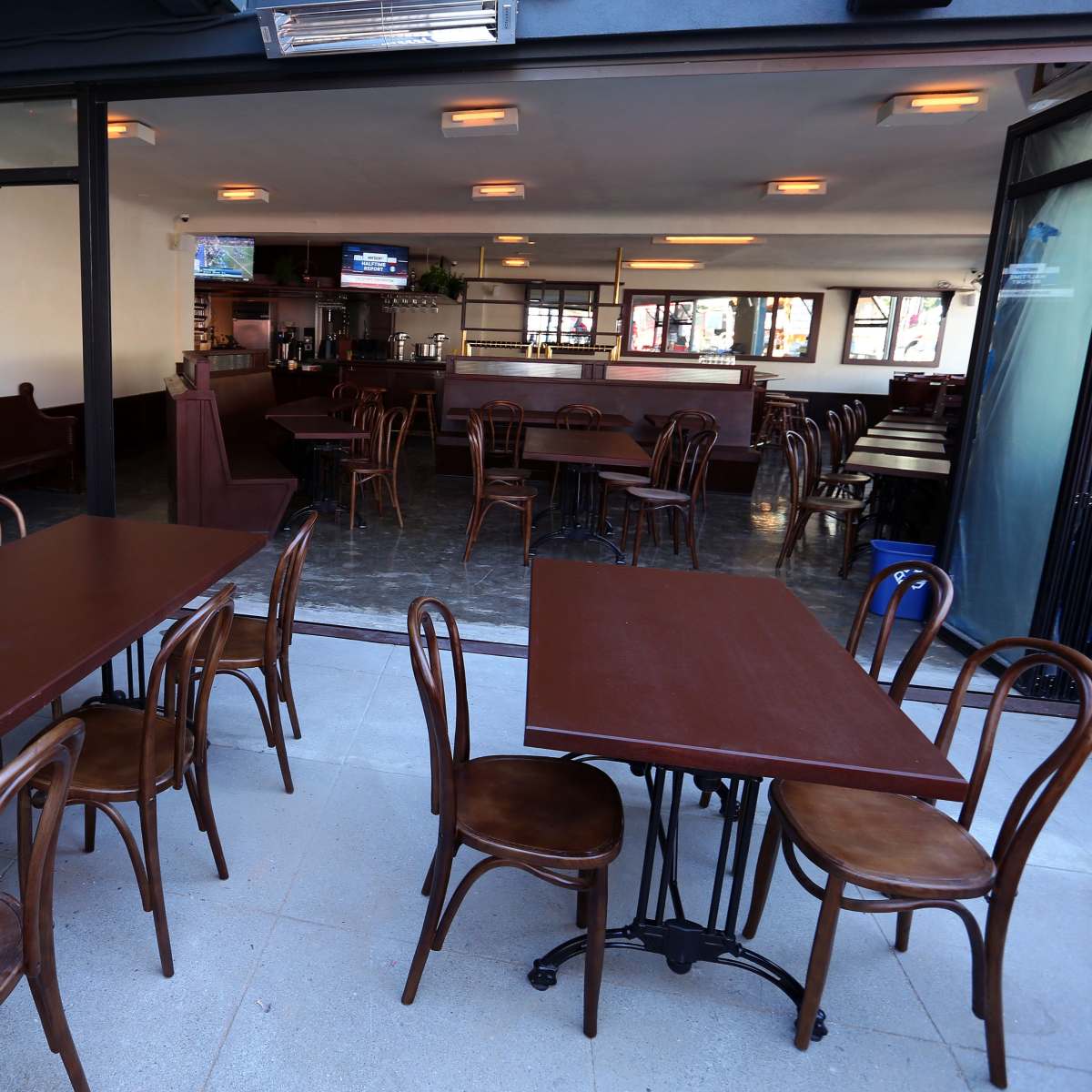 A partially open restaurant with several empty wooden tables and chairs arranged inside.