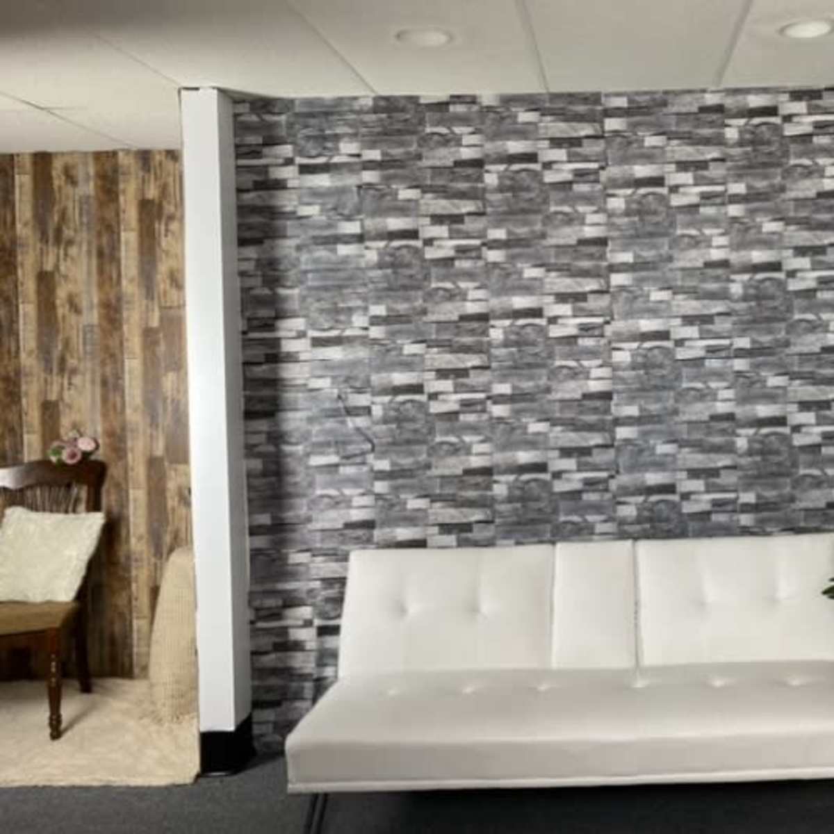 A sleek white futon against a patterned grey wall, with a newspaper-covered wall on one side and a potted plant nearby.
