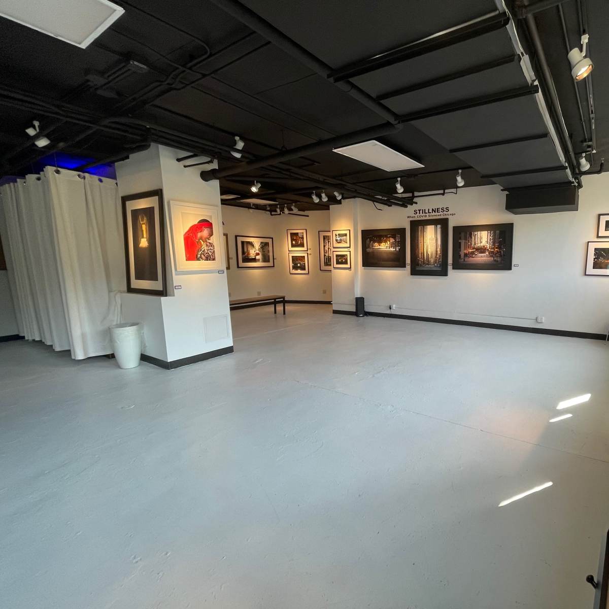 A spacious art gallery with white walls, featuring framed photographs displayed throughout the exhibit.