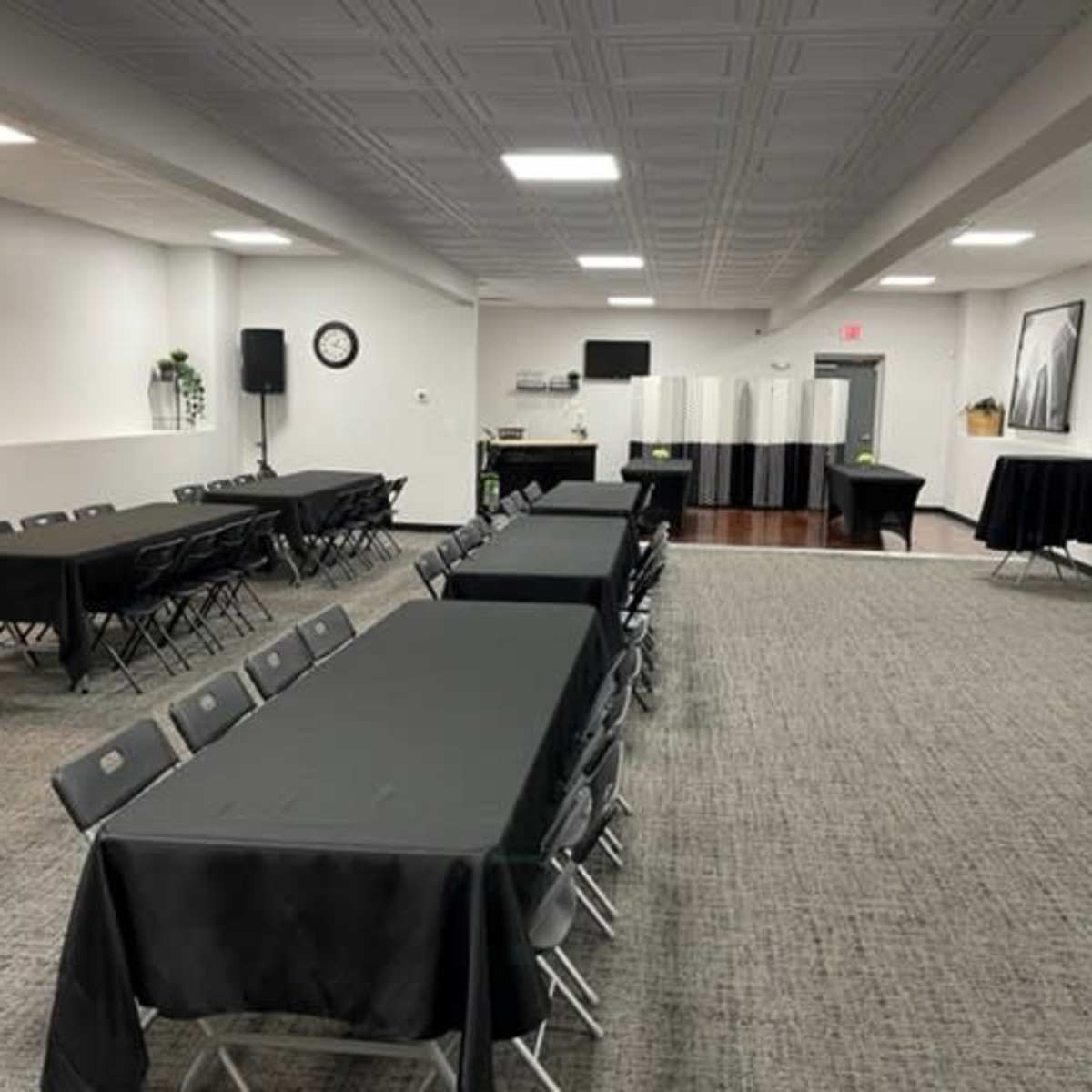 A large, empty event space with multiple black-covered tables arranged in rows and a few round tables set up along the perimeter.