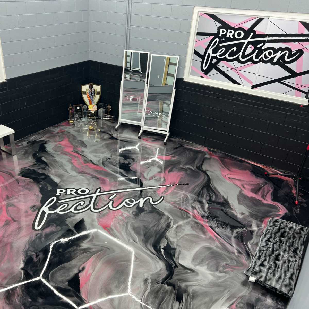 A corner of a room with a patterned black and pink floor, a white bench, a mirror, and various objects displayed on shelves.