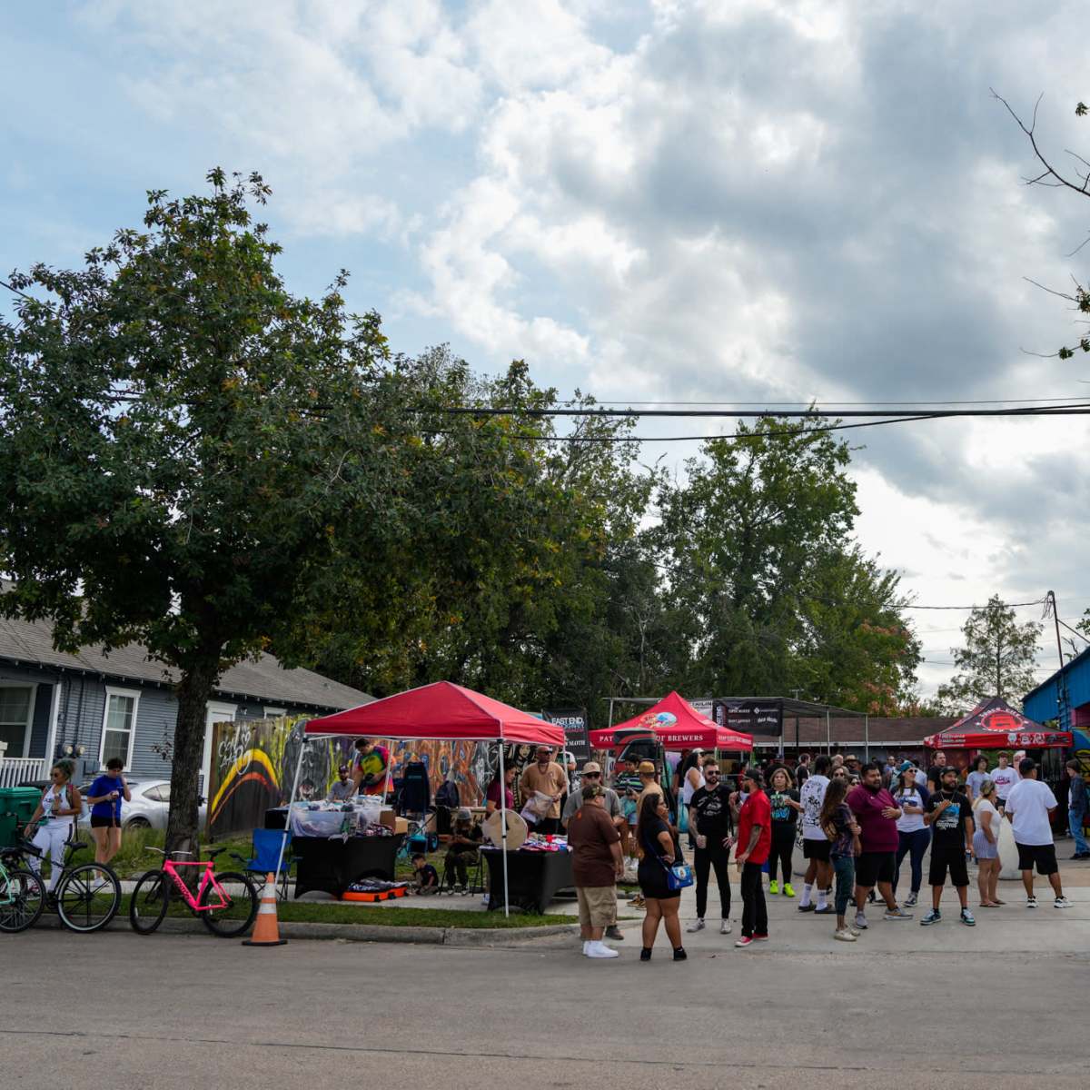 A crowd gathers at an outdoor event with tents and activities in front of a building under a cloudy sky.