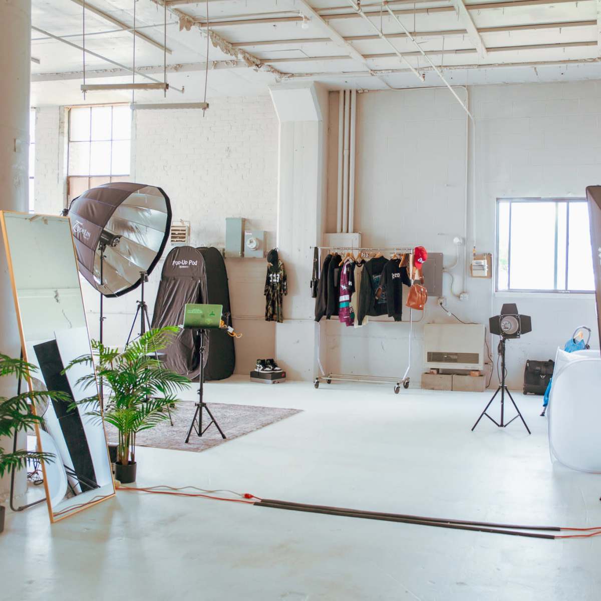 A spacious photography studio featuring softbox lights, a large mirror, clothing racks, and a projector on a stand.