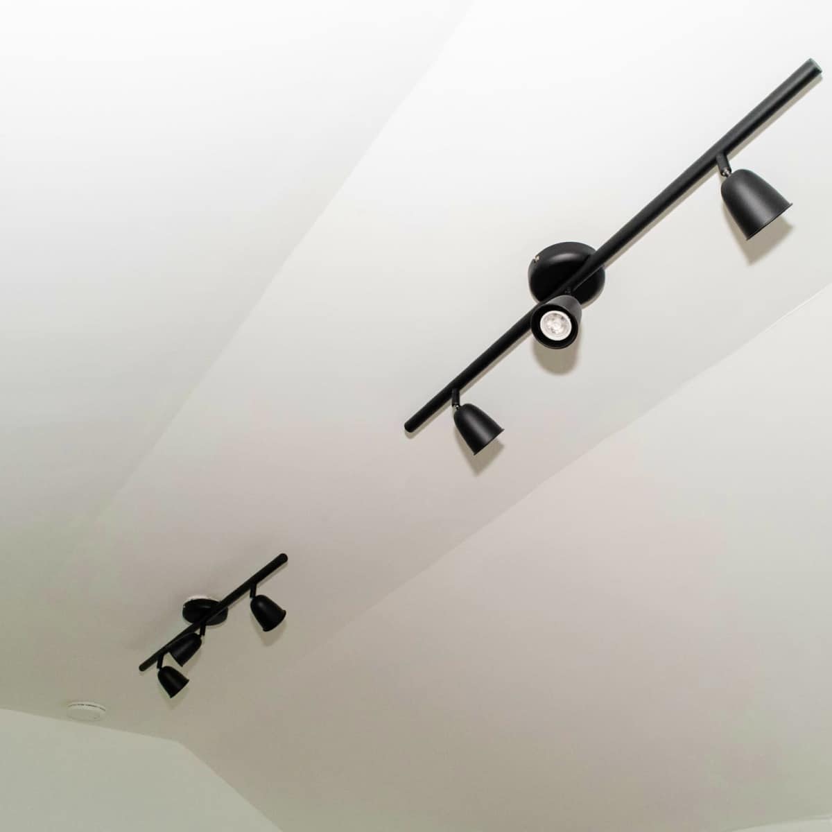 Two black track lighting fixtures mounted on a white ceiling.
