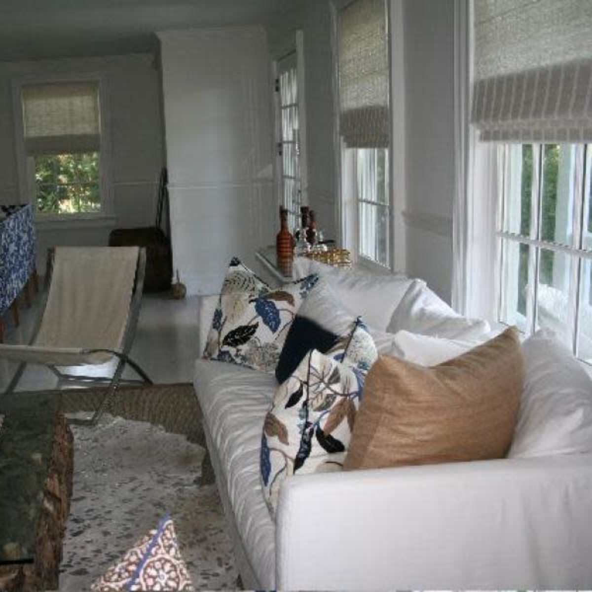 A living room with a white sofa, a glass coffee table, and large windows allowing natural light to enter the space.