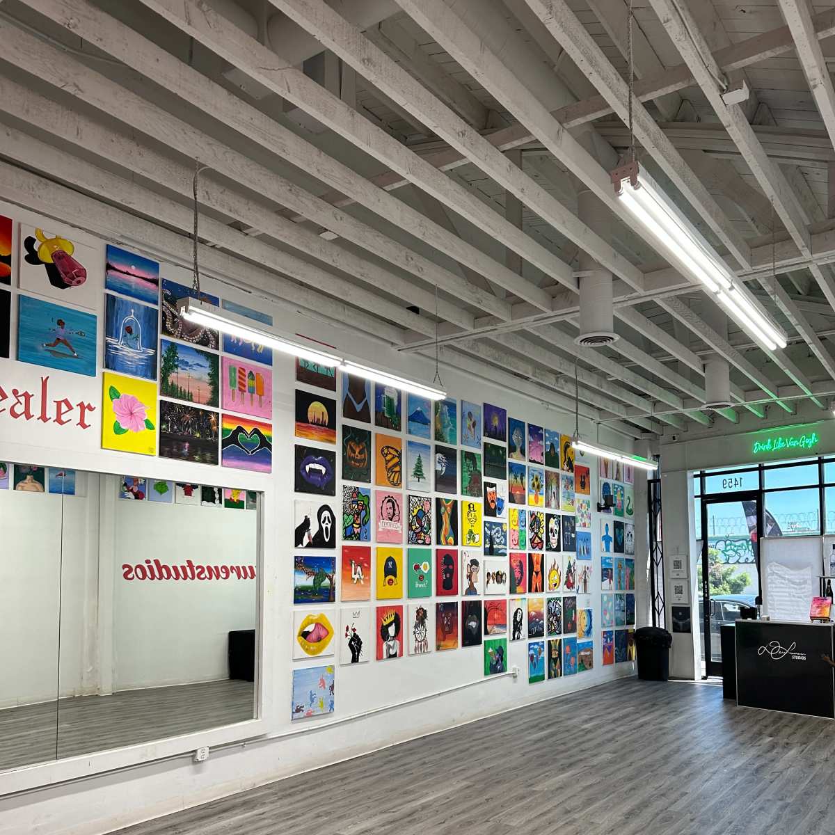 A brightly lit studio with a wall covered in colorful artwork and a large mirror on the opposite side.