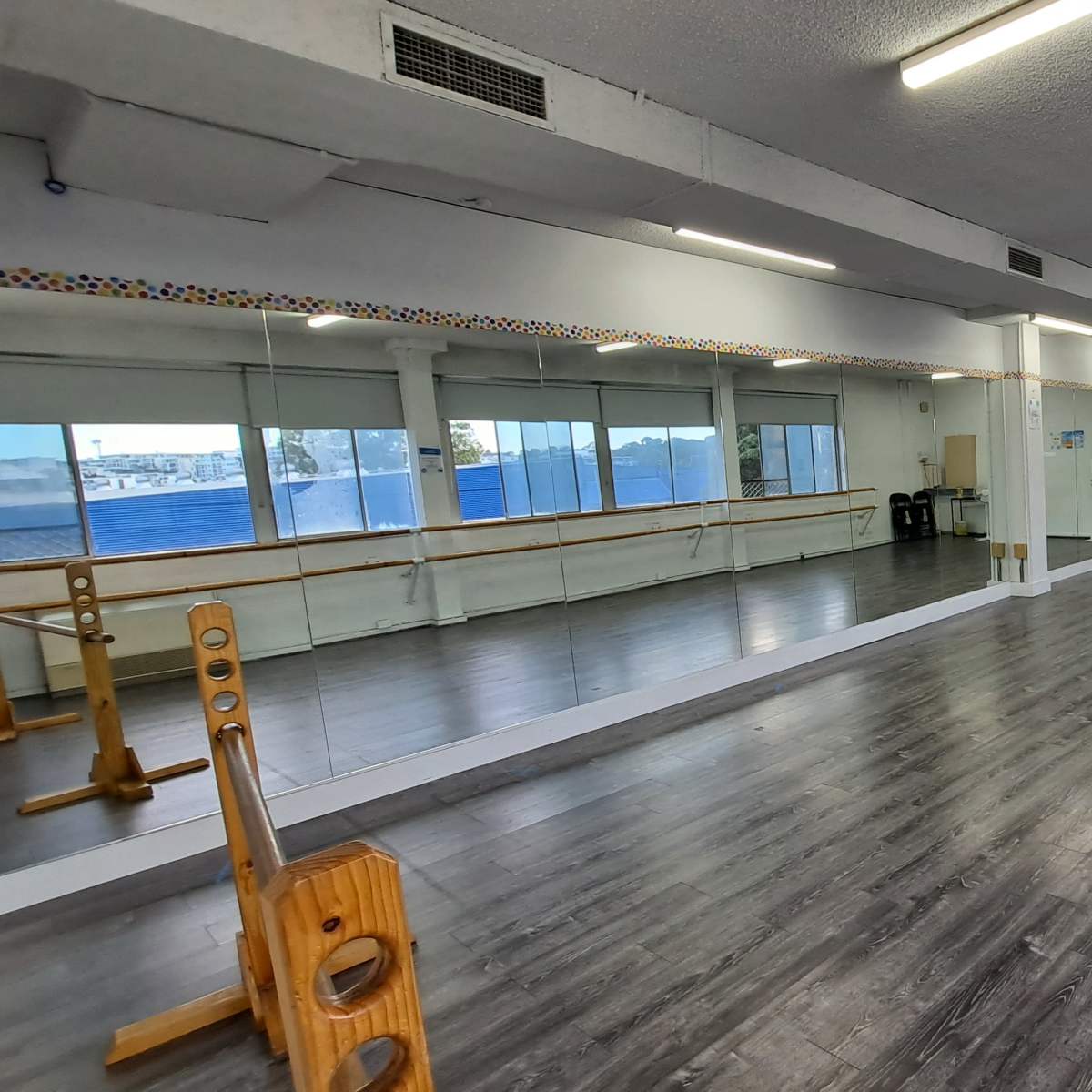 A bright, spacious dance studio with mirrors along one wall and a wooden ballet barre.
