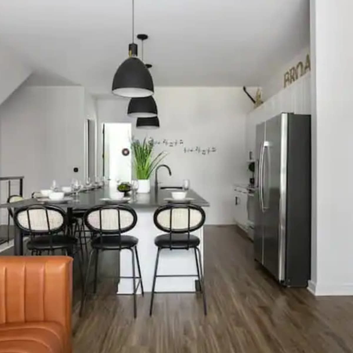 A modern kitchen features a central island with bar stools, stainless steel appliances, and a patterned accent wall.