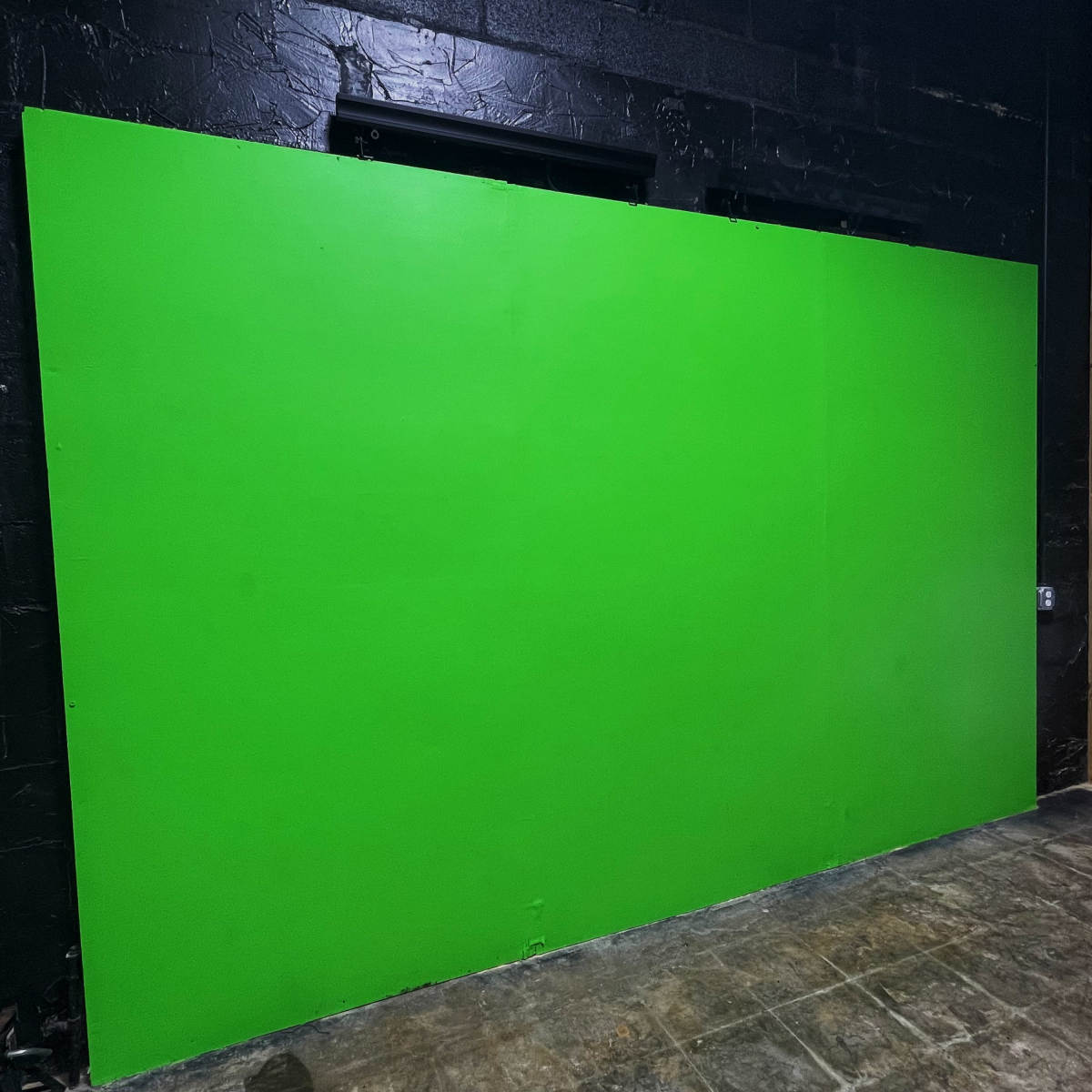 A large green wall in a dimly lit room with a concrete floor.