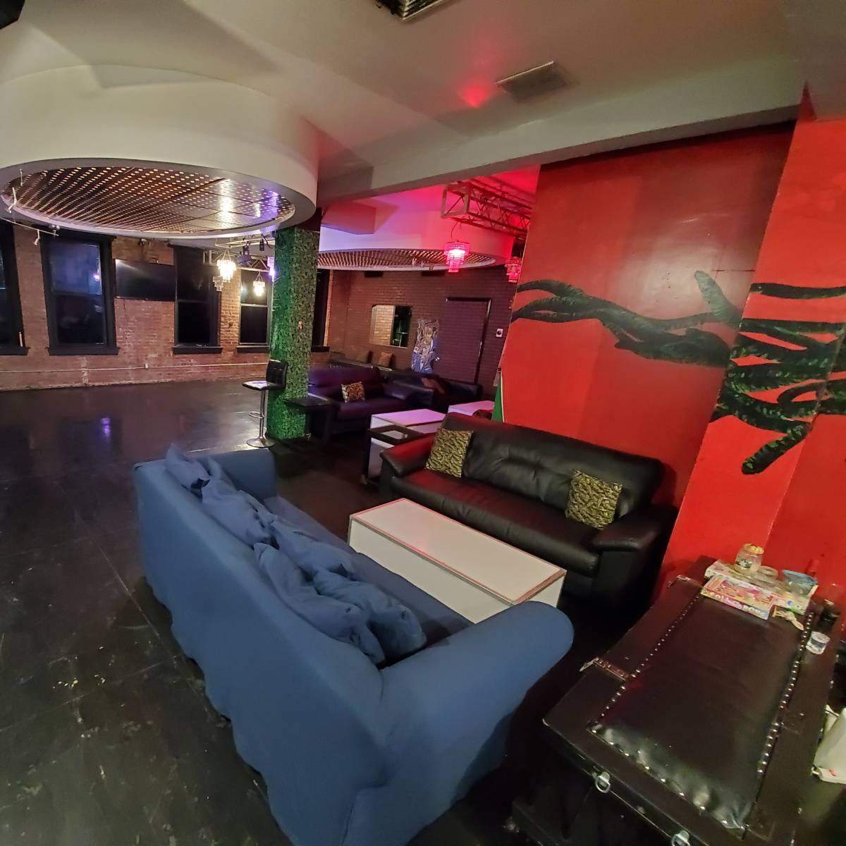 A spacious indoor lounge area featuring dark flooring, various seating arrangements, and a red accent wall with artwork.