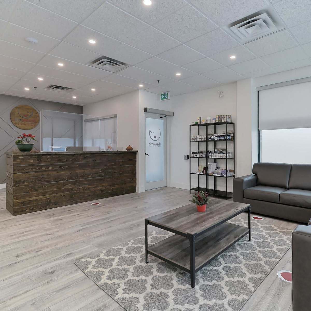 A modern waiting area with a reception desk, a gray sofa, a coffee table, and a shelf filled with various items, all arranged in a well-lit space.