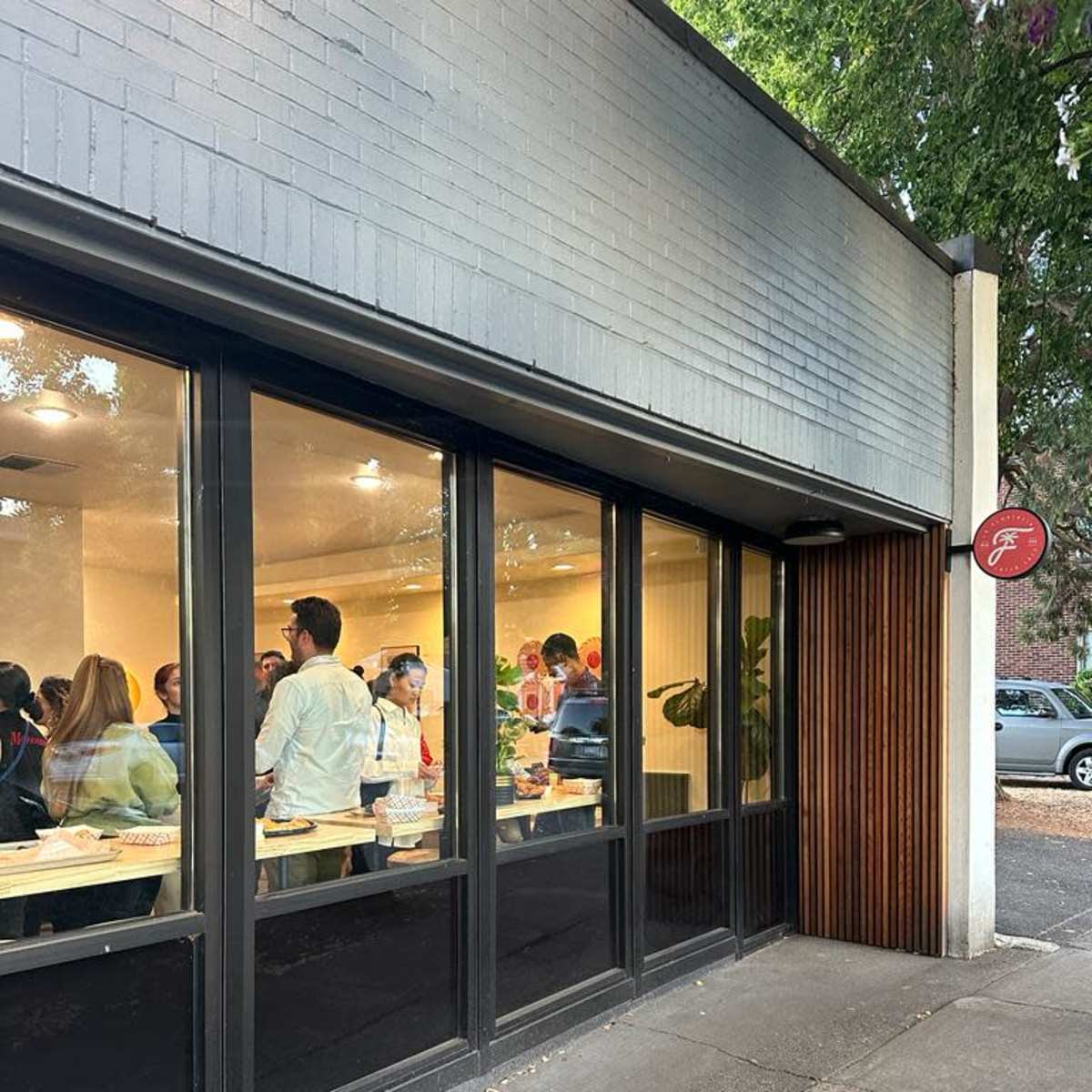 A group of people is gathered inside a modern cafe, as seen through large windows.