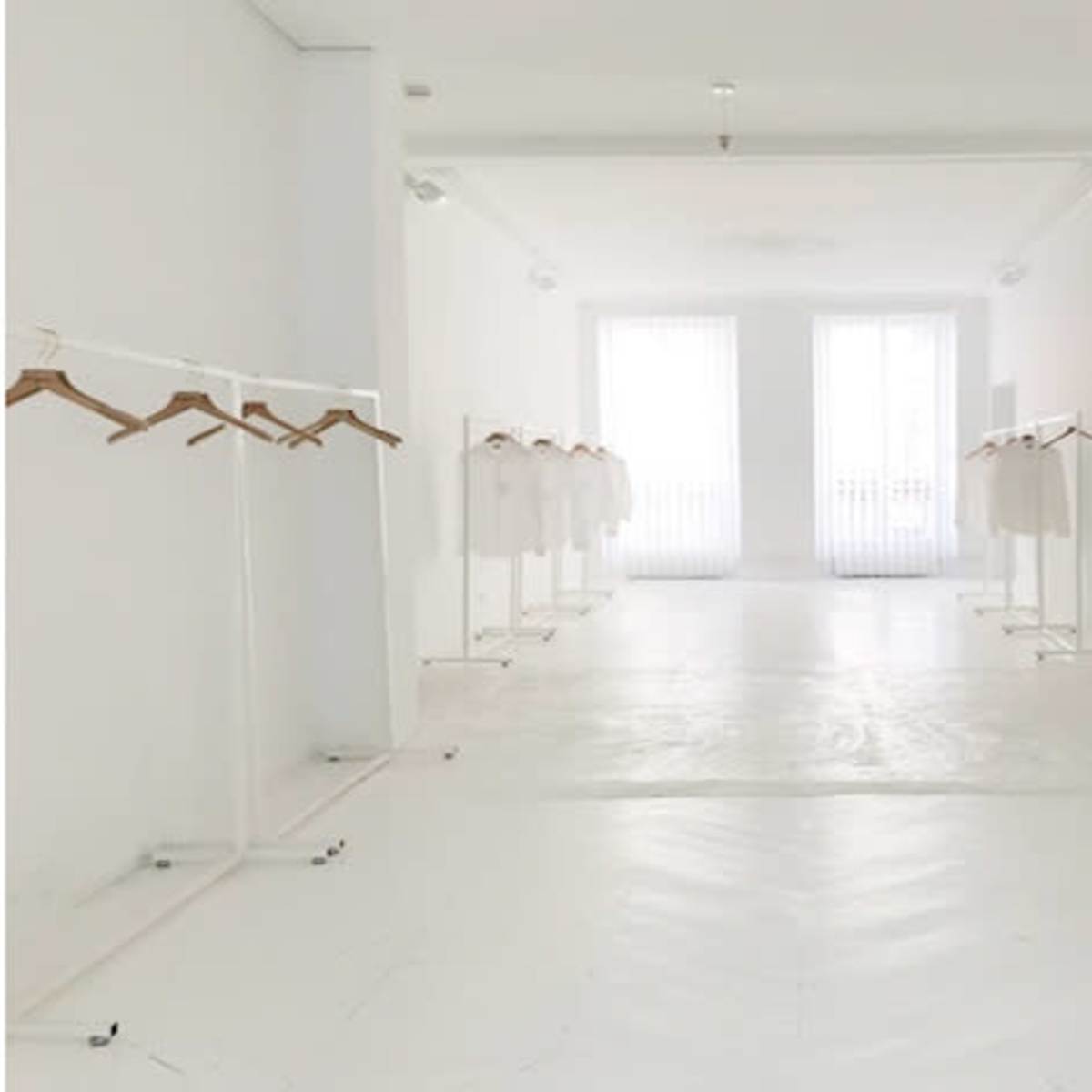 A minimalist, white interior space with clothing displayed on hangers arranged in rows.