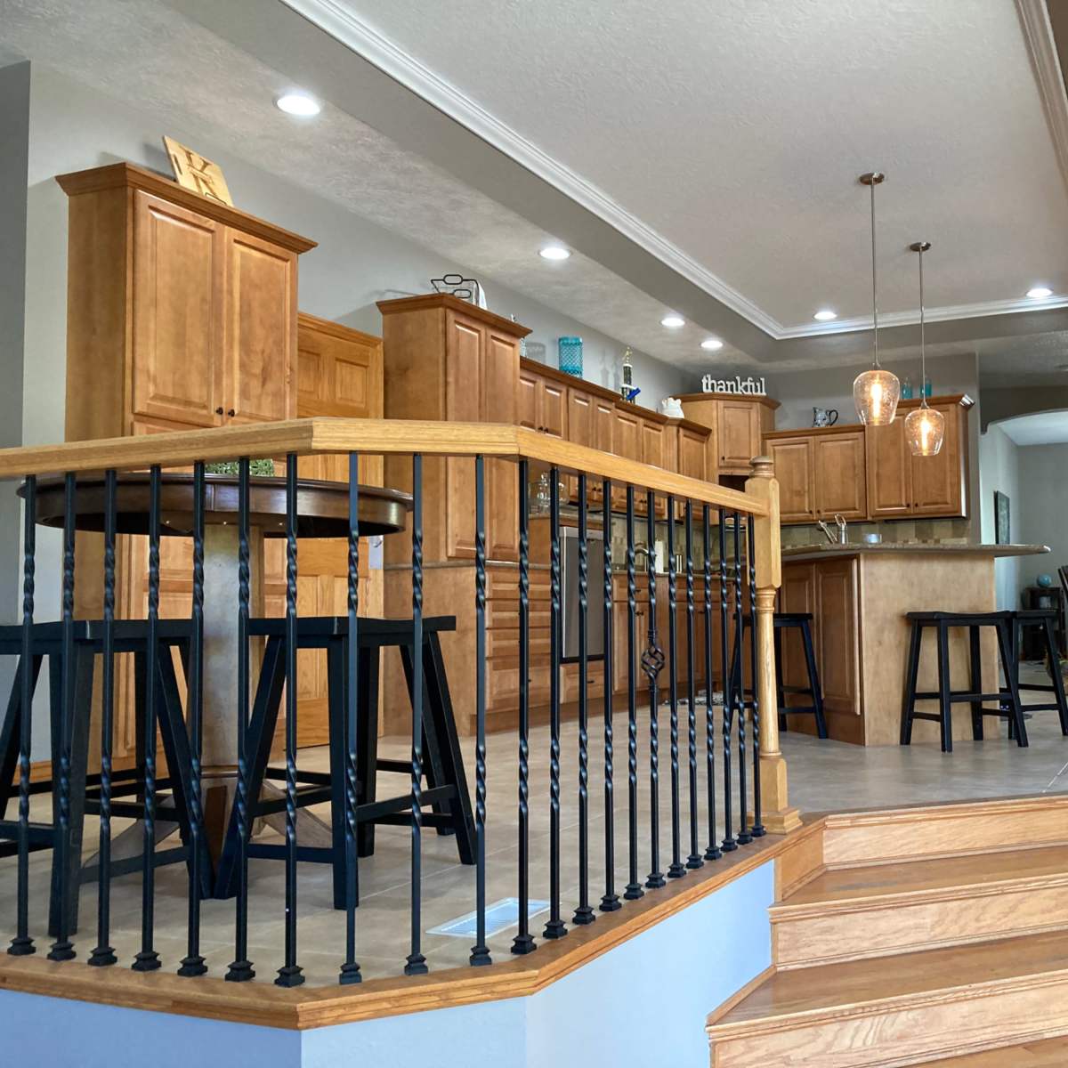 A staircase leads to an open kitchen with wooden cabinets, a large island, and modern lighting fixtures.