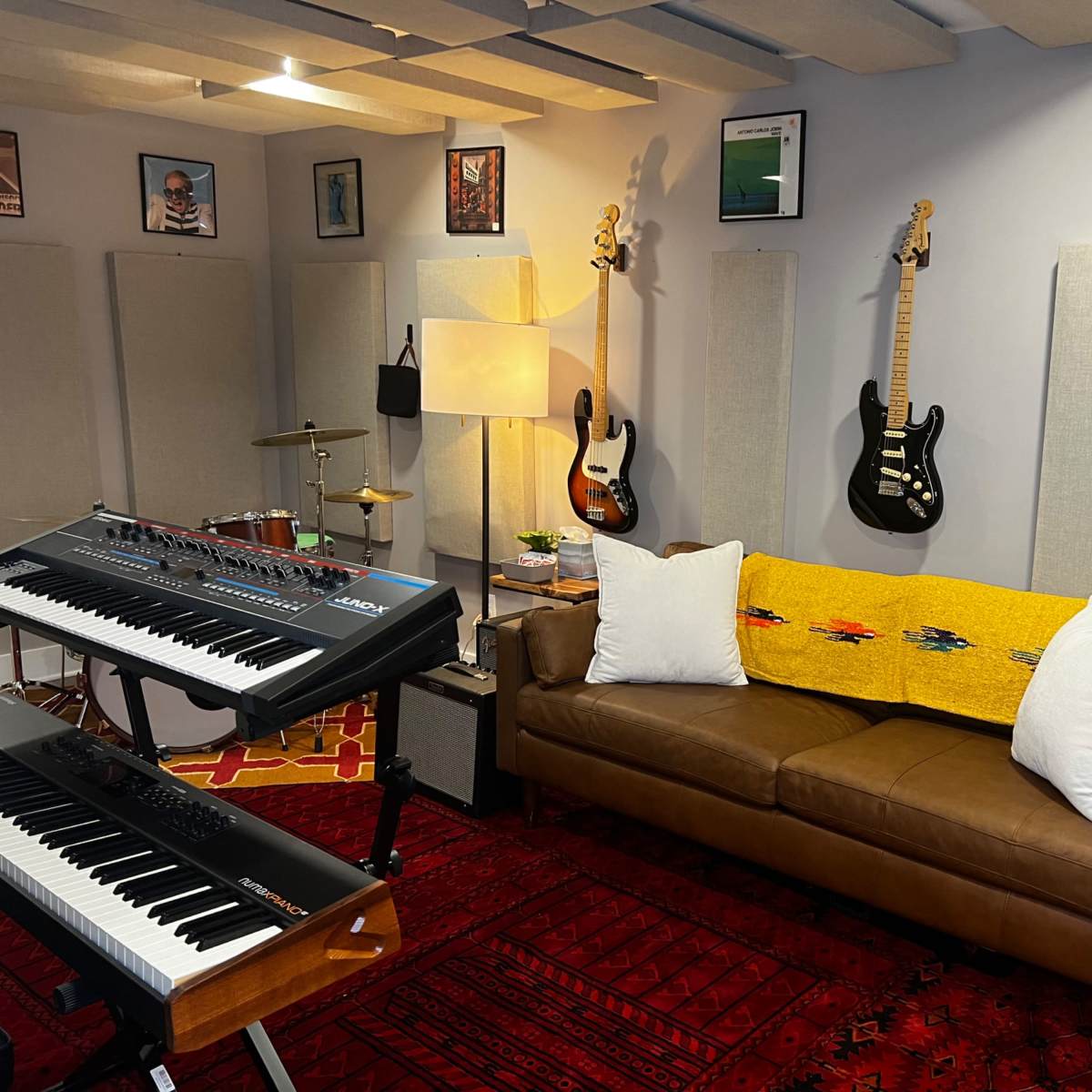 A cozy music studio with a brown sofa, musical instruments including guitars and keyboards, and various framed artworks on the walls.
