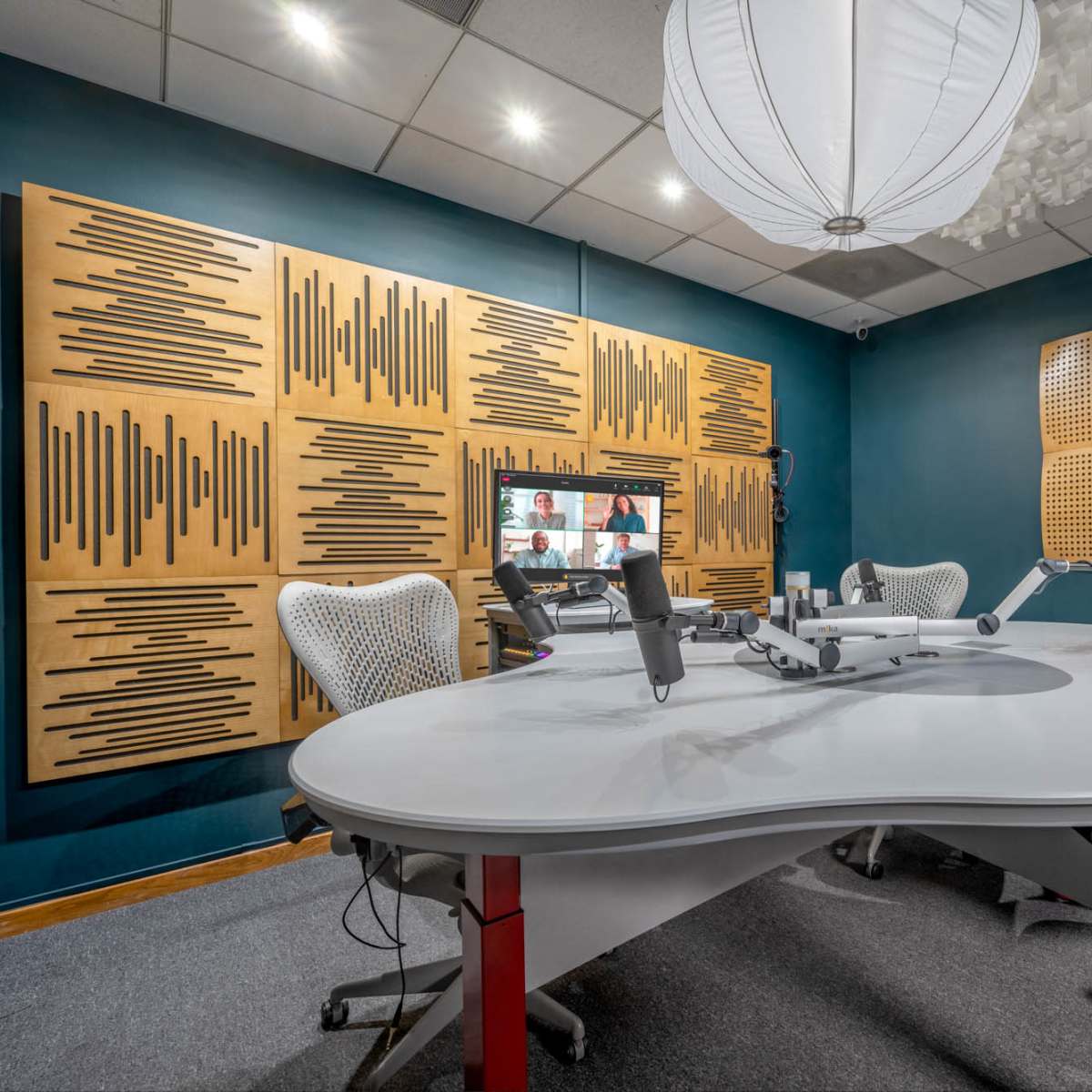 A modern recording studio with a large white table, ergonomic chairs, and sound-absorbing wall panels.