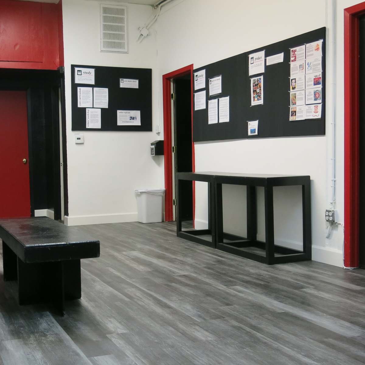 A waiting area with a row of black chairs, a long black table, and bulletin boards on the walls.
