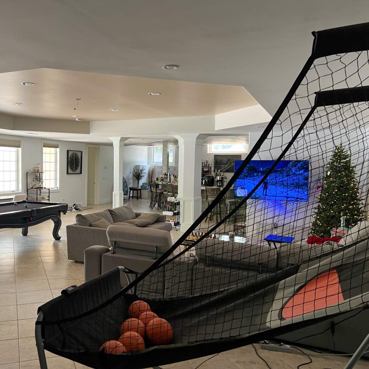 A spacious living room featuring a pool table, a large television, a basketball shooting arcade game, and a Christmas tree in the corner.