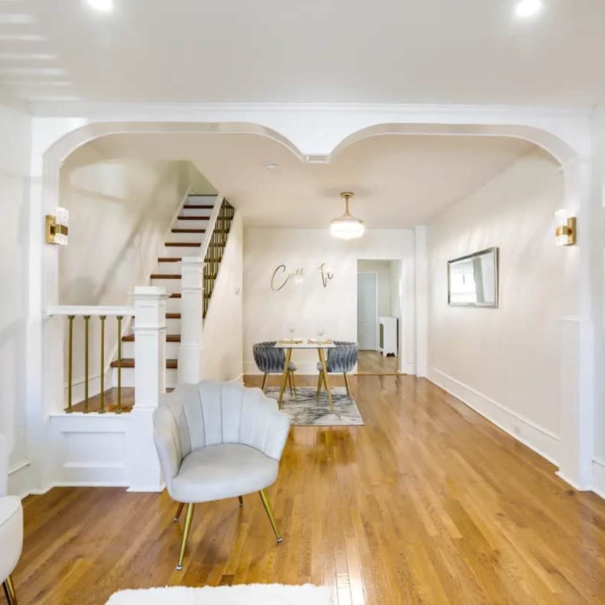 A spacious living area featuring a staircase, a dining table with chairs, and a mounted television on a white wall.