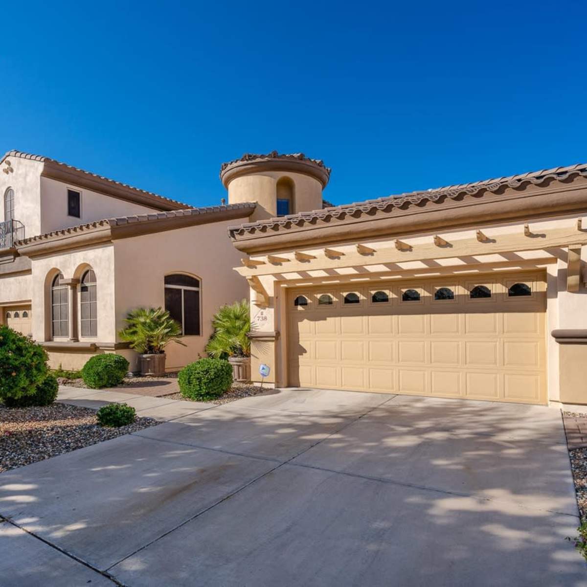 A two-story house with a tile roof, a curved turret, and a large garage is set in a well-landscaped yard.