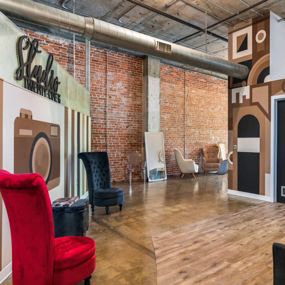 A modern interior space with exposed brick walls, artistic mural designs, and a mix of stylish furniture, including a red and a black chair.