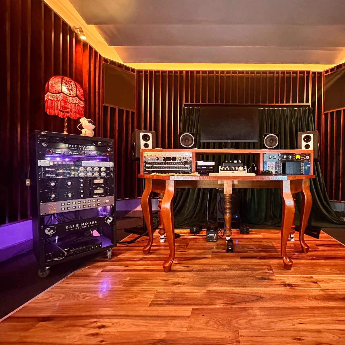 A music production studio featuring a wooden table with audio equipment, surrounded by sound panels and various music instruments.