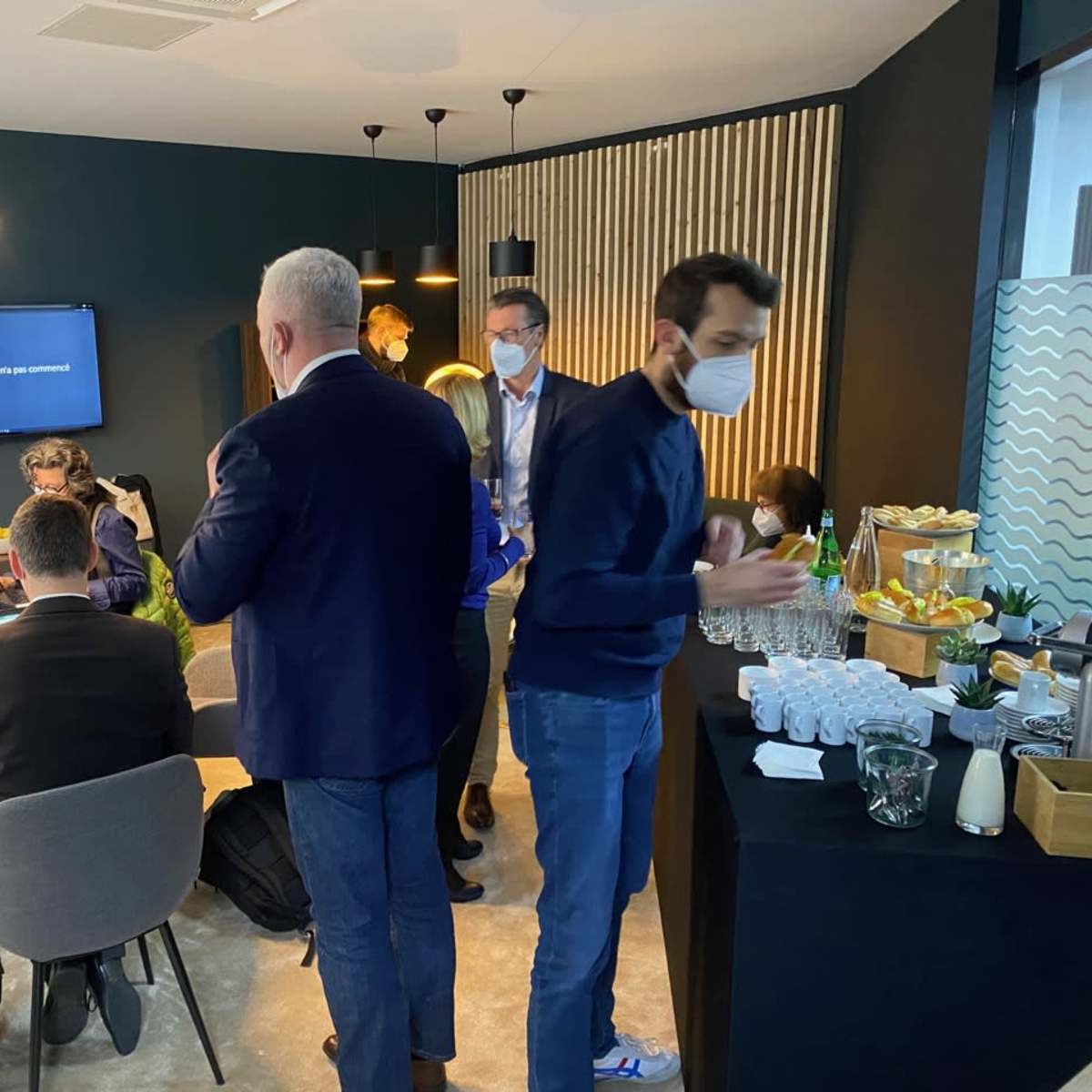 A group of people are engaged in conversation and activities in a modern meeting room, with a buffet table set up in the corner.