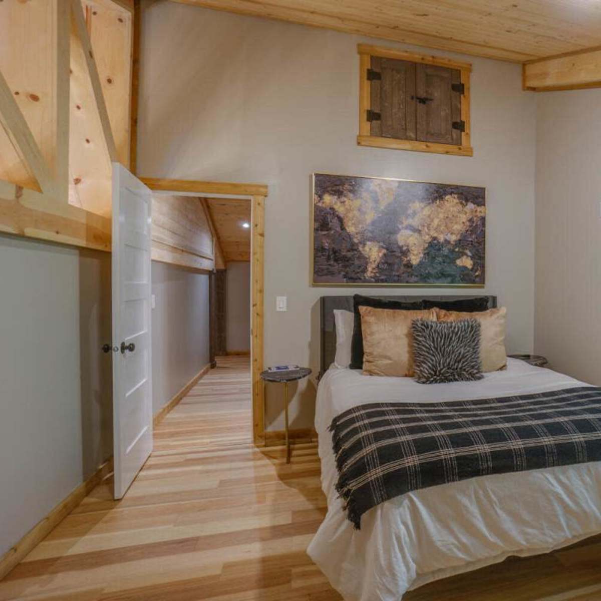 A small bedroom features a bed with a plaid throw, a world map on the wall, and a window overlooking a wooded area.